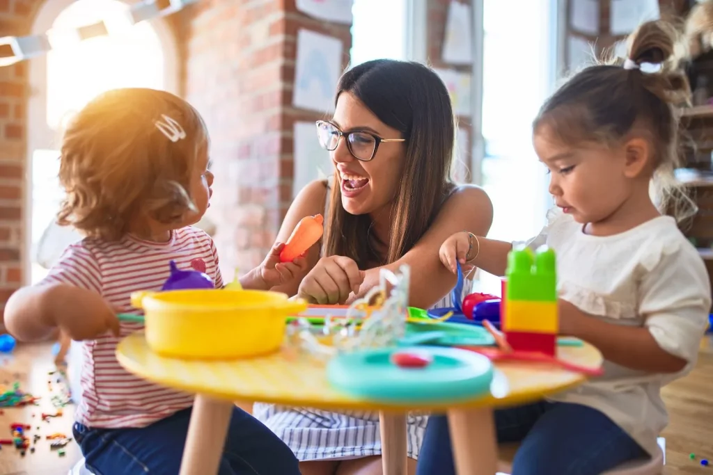 Image of young children sitting on the floor in a colorful classroom setting with a teacher.